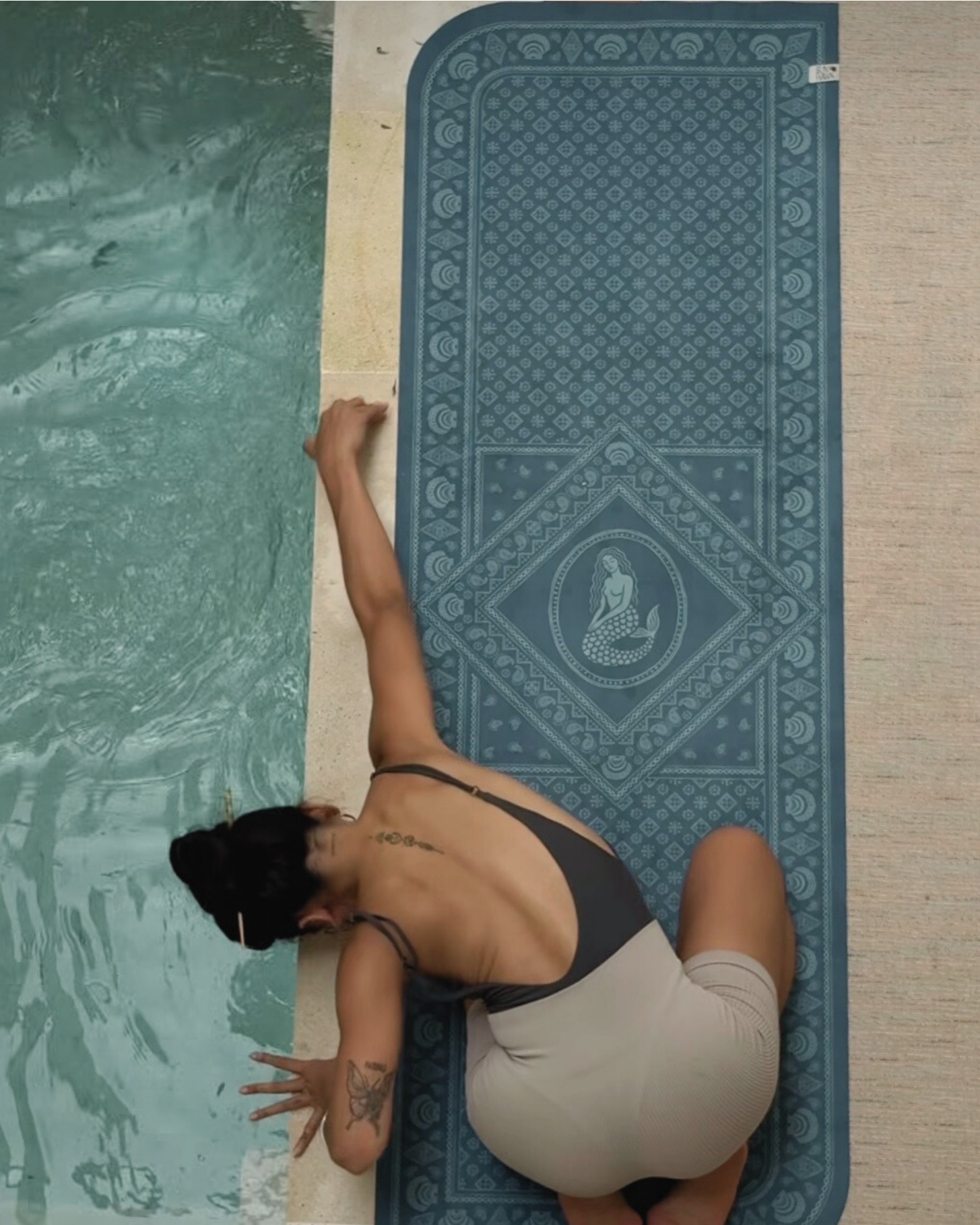 Person in a swimsuit on a SunHawk travel yoga mat by a pool