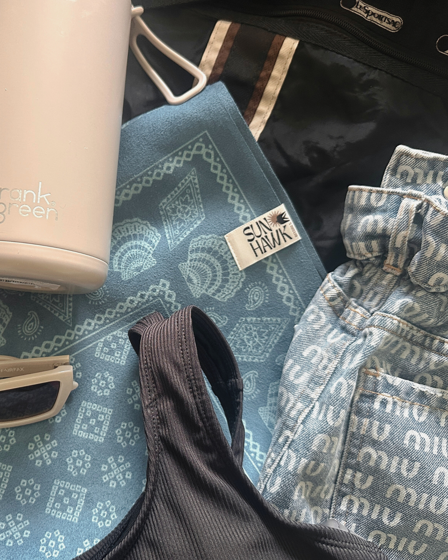 Collection of clothing and accessories including a blue patterned yoga mat, water bottle, activewear  and denim jeans on a gym bag